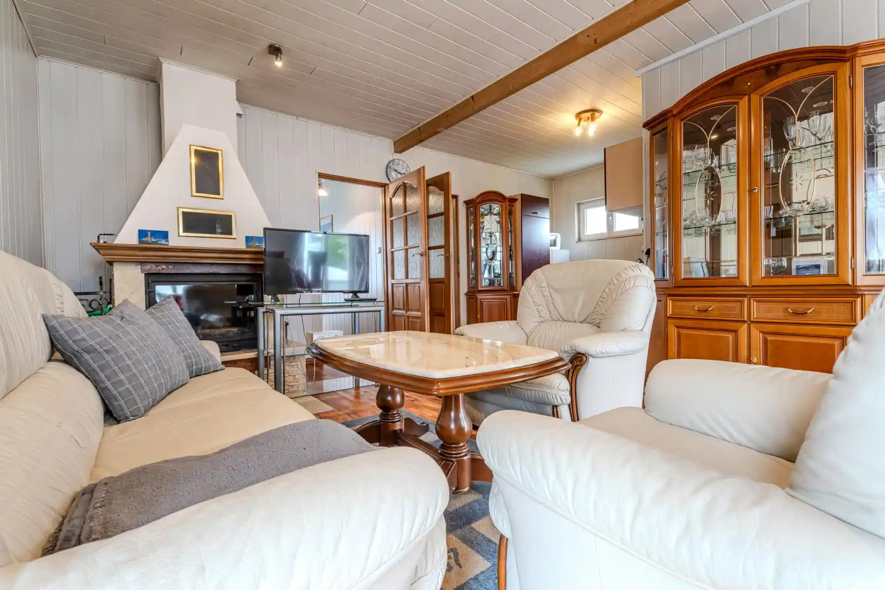 Auf diesem Bild sehen Sie das Wohnzimmer mit Couch-Garnitur, Anbauwand, Fernseher, Kamin sowie Zugängen zu den Schlafzimmern und der Küchenzeile des Ferienhauses der Villa See-Eck im Seebad Ahlbeck auf der Insel Usedom von https://aufnachusedom.de.
