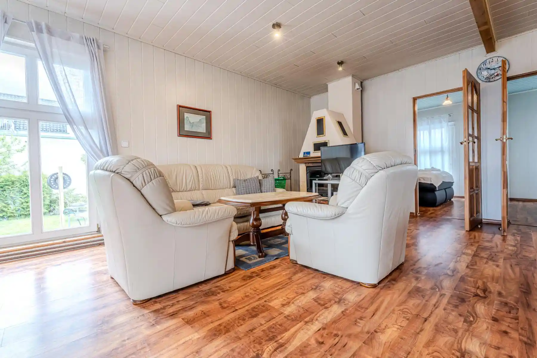 Auf diesem Bild sehen Sie das Wohnzimmer mit Couch-Garnitur, Anbauwand, Fernseher, Kamin sowie Zugängen zu den Schlafzimmern des Ferienhauses der Villa See-Eck im Seebad Ahlbeck auf der Insel Usedom von https://aufnachusedom.de.