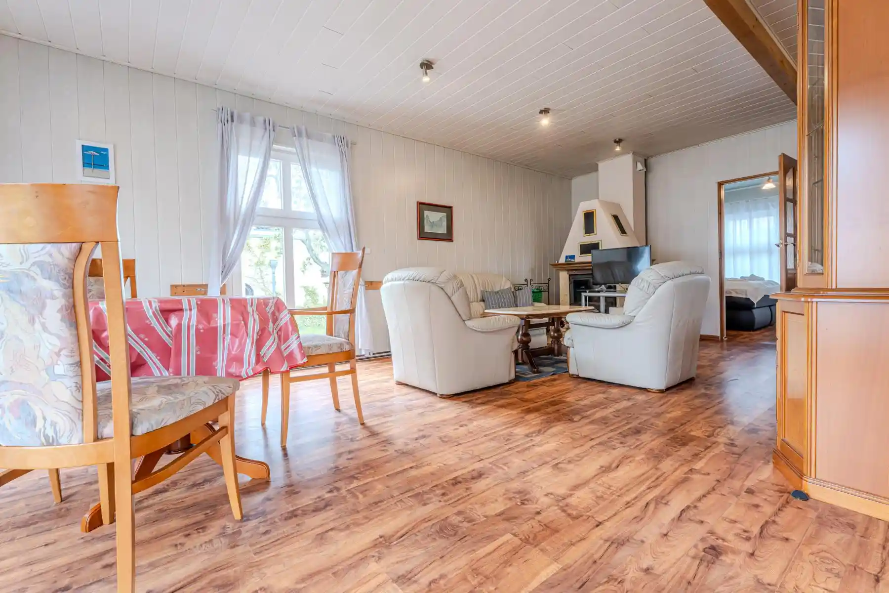 Auf diesem Bild sehen Sie das Wohnzimmer mit Esstisch, Couch-Garnitur, Anbauwand, Fernseher, Kamin sowie Zugängen zu den Schlafzimmern des Ferienhauses der Villa See-Eck im Seebad Ahlbeck auf der Insel Usedom von https://aufnachusedom.de.