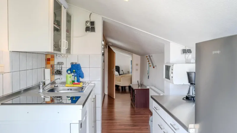 Auf diesem Bild sehen Sie die Küchenzeile mit Kühlschrank, Geschirrspüler, Mikrowelle, Mini-Backofen der Ferienwohnung Seepferdchen im ersten Obergeschoss des Gästehauses der Villa See-Eck im Seebad Ahlbeck auf der Insel Usedom von https://aufnachusedom.de mit Blick auf den Zugang zu einem der Gästezimmer.